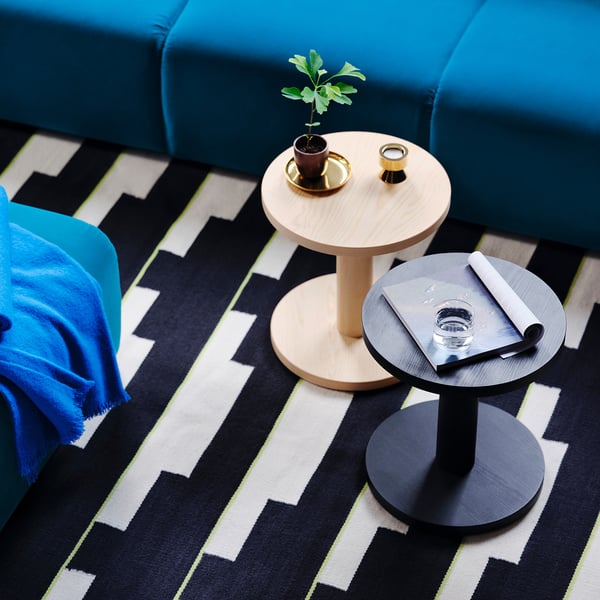 Blue sofa with two side tables. One holds a plant, the other has a glass and notebook. Black and white zigzag rug underneath.