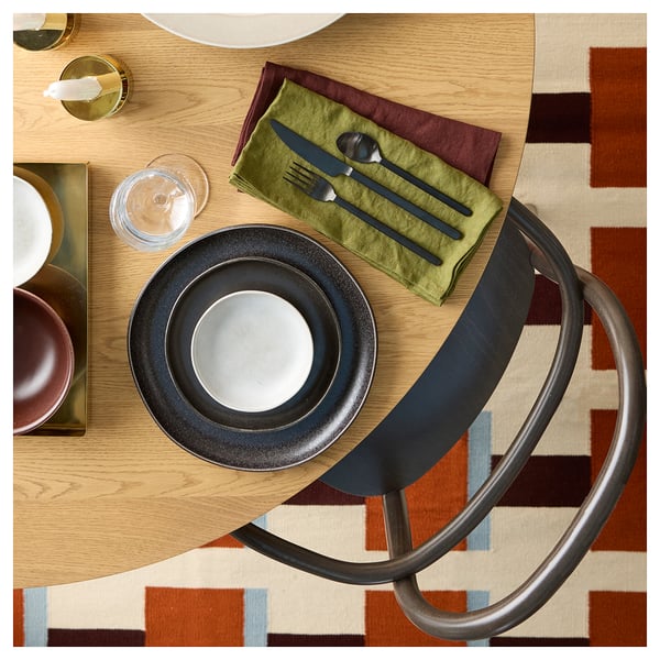 A geometric, handwoven wool rug in brown and beige on a wooden table with place settings.
