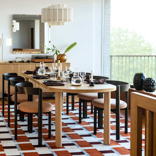 Modern dining setup with wooden table, black chairs, pendant light, colourful rug, and decor.