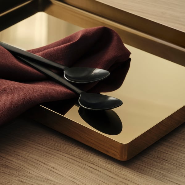 A sleek, modern tray with dark handles on a wooden table, accompanied by dark utensils and a maroon cloth.