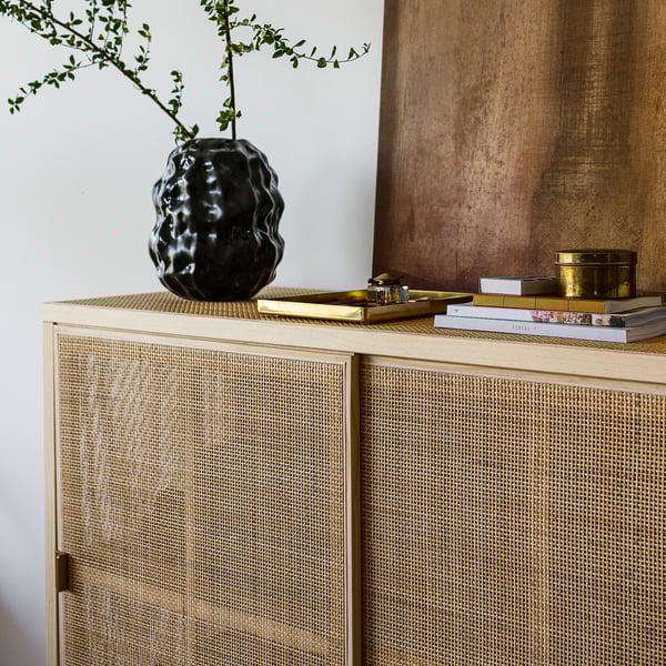 A stylish, textured stoneware vase on a wooden cabinet, holding fresh greenery.