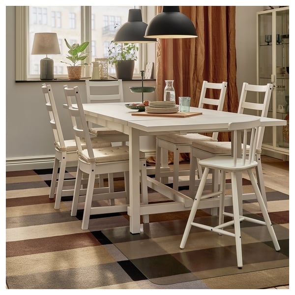 Cosy dining area with wooden table, chairs, rug, lamp, plants, and tiered tray.