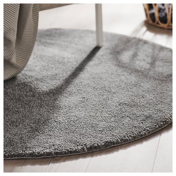 Grey circular rug with a thick, soft pile lies on a wooden floor, partially under a striped chair.