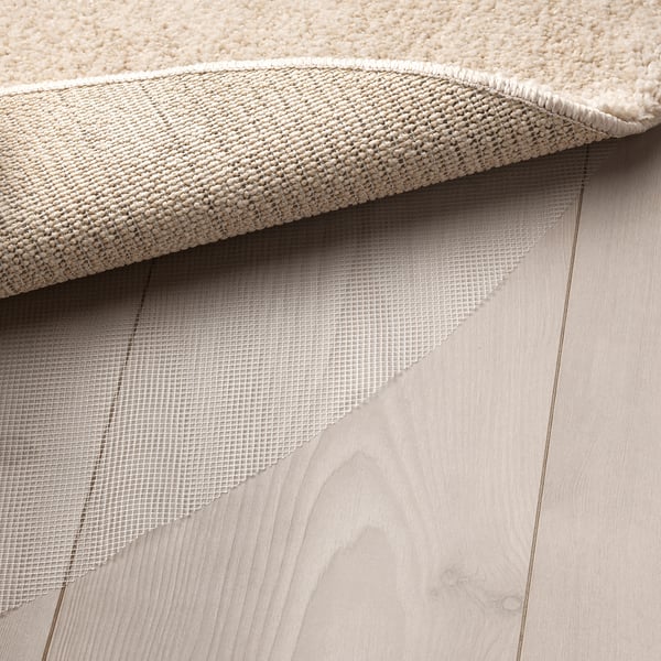 Close-up of plush rug on wood floor, showcasing thick pile and underside mesh, emphasising comfort and stability.