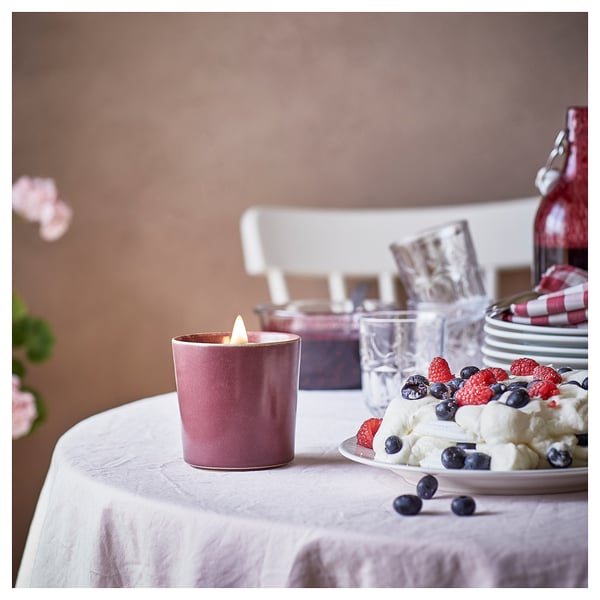 A lit pinkish-purple STÖRTSKÖN candle, made of ceramic, on a table with berries and cream.