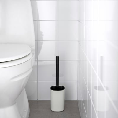 White toilet brush in black holder beside a toilet in a minimalist bathroom.