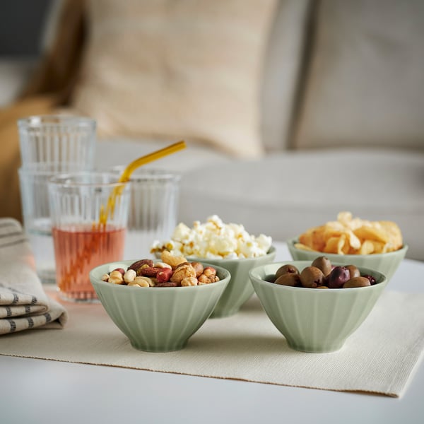 Four green bowls with snacks. Floral patterns, scandinavian-japanese inspired. On beige tablecloth with drinks.