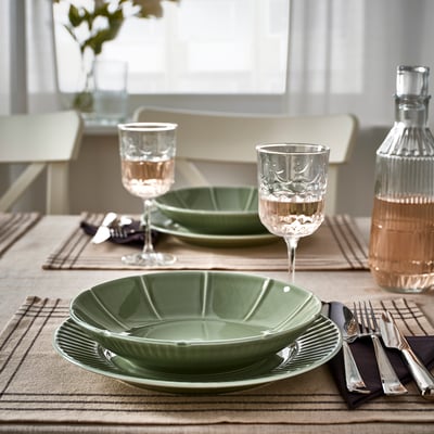 Green STRIMMIG bowls and plates on table with cutlery and glasses.