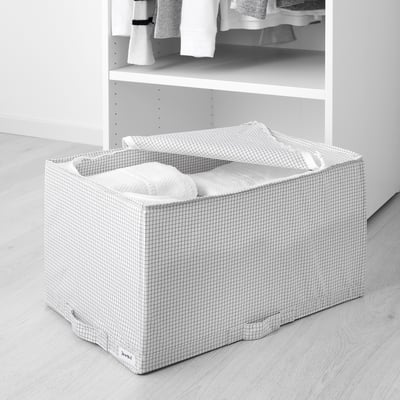 White grid storage box with handles on floor, holding folded clothes, part of STUK series for dust protection and air circulation.