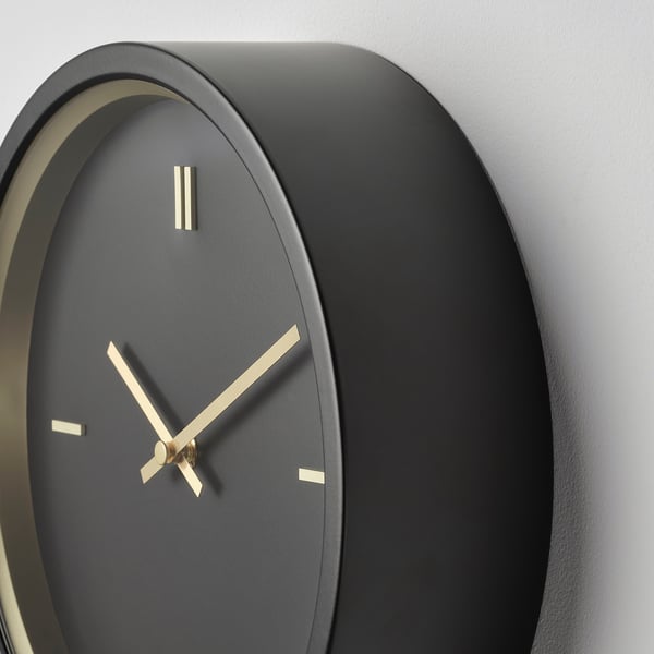 Modern wall clock with dark face, golden hands, and simple design. Elegantly mounted on a plain wall.