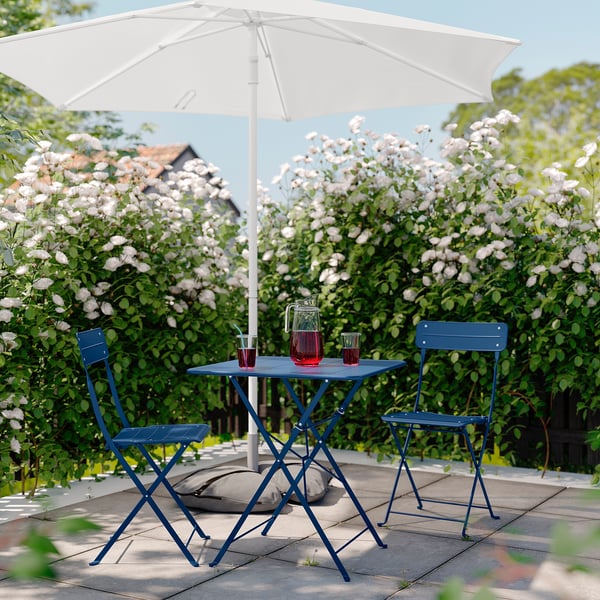 Blue metal patio set with table and chairs under a white umbrella, set in a lush garden.