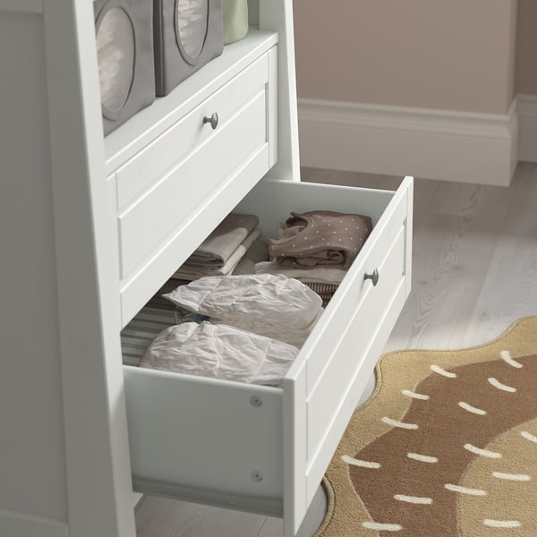 Open white chest drawer, neatly storing folded baby clothes and diapers. Safe, organised nursery furniture.