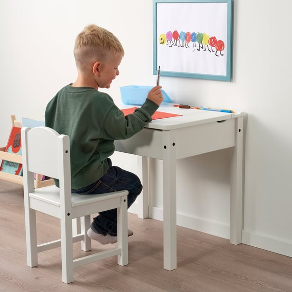 Kid drawing at desk, chair, with art supplies and books.