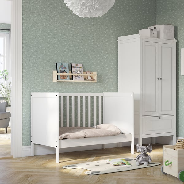 White SUNDVIK baby cot with nursery items, green wallpaper, wardrobe.