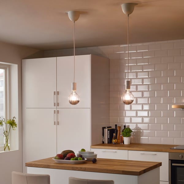 Modern kitchen: white cabinets, wood counter, pendant lamps, fruit bowl, window.