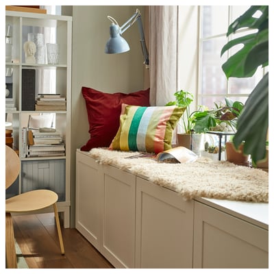 Cosy room with white bench, colourful pillows, plants, books, and a fluffy white SVINDINGE rug.