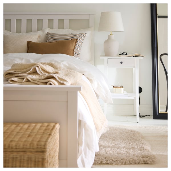 Neutral bedroom with white bed, throw pillow, wicker basket, and fluffy beige rug.