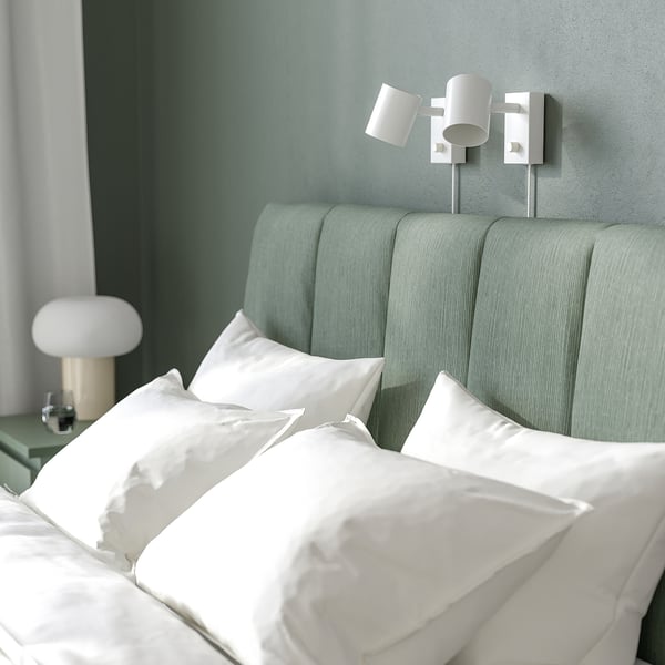 Adjustable bed with comfy headboard and clean lines. Made with white sheets and green accents. Two wall lamps.