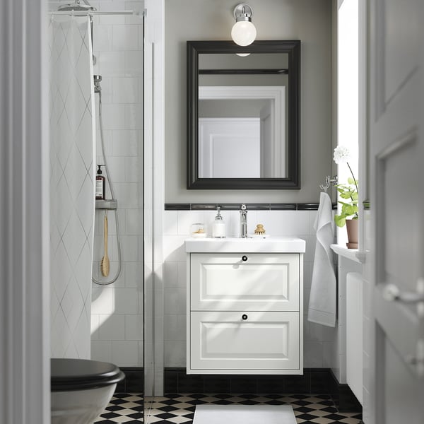 Modern bathroom: white cabinet, large mirror, black shower, black-and-white floor, sink with drawers, towels, plants.
