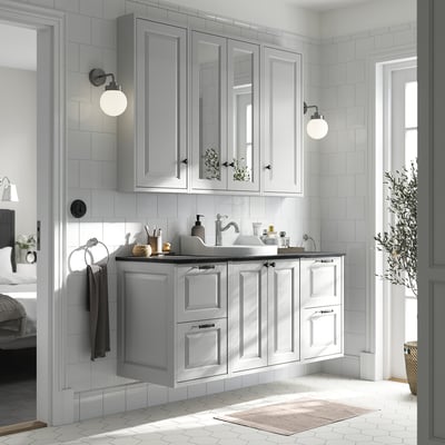 Modern bathroom with light grey TÄNNFORSEN cabinet set, marble counter, wall lamps, and plant.