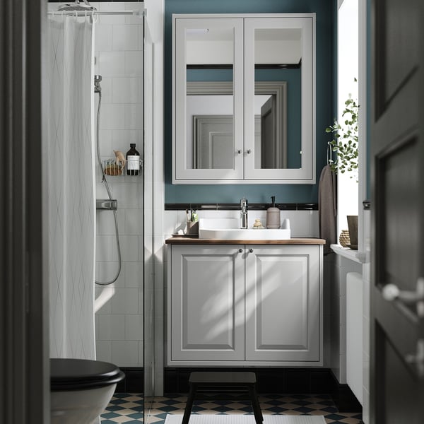 Modern bathroom with grey TÄNNFORSEN vanity, light blue accents, white sink, and black & white patterned floor.