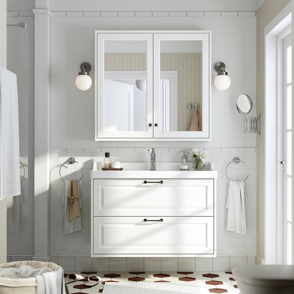 White TÄNNFORSEN bathroom vanity with bevelled edges, two drawers, ceramic sink, large mirror, and wall lights.