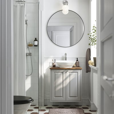 Modern bathroom with grey TÄNNFORSEN vanity, white sink, mirror, and glass shower door.