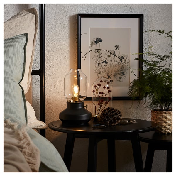 Black lamp on table, warm light. Frame floral art, dried plants, sphere decor.