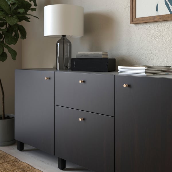 Modern grey cabinet with oak knobs, topped with lamp, books, and speaker.