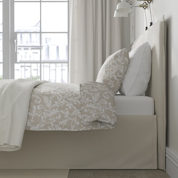 Modern bed by window, soft headboard, removable cover, light beige pattern, white pillows, curtains, city view.