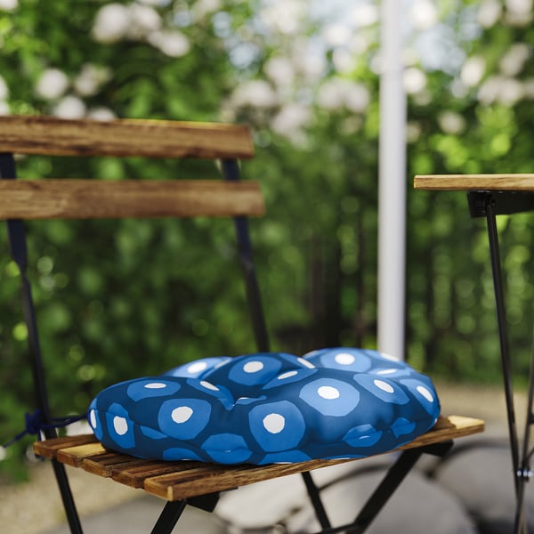 Blue patterned cushion on wooden chair in outdoor setting.
