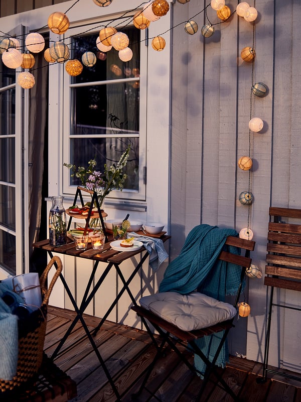 Cosy balcony with TÄRNÖ outdoor furniture, string lights, and teal blanket.