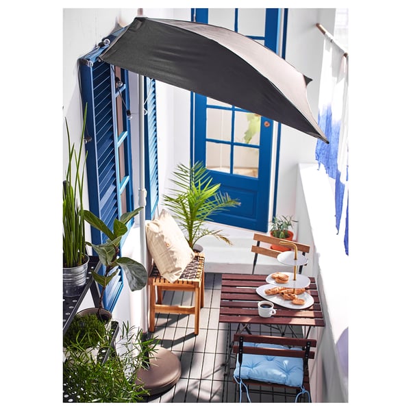 Balcony setup with TÄRNÖ foldable wooden table, grey parasol, blue pillows, plants, and food.