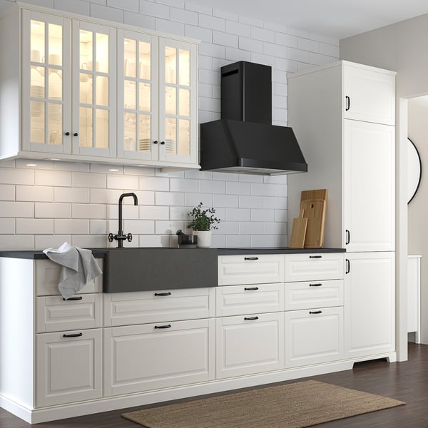 Modern white kitchen with dark grey quartz sink. Glass-front cabinets, black hood, and stainless tap. Note the unique tall cabinet.