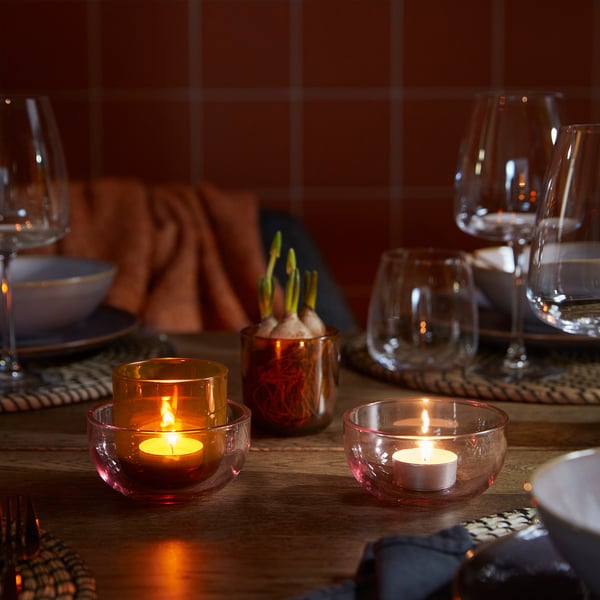 Wooden table set with tealights, glasses, and flowers, creating a warm, intimate dining atmosphere.