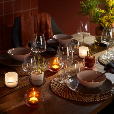 Elegant dining setup with TALLTITA glass tealight holders in warm colours. Candles, bowls, and vases on a wooden table, creating a cosy ambiance.