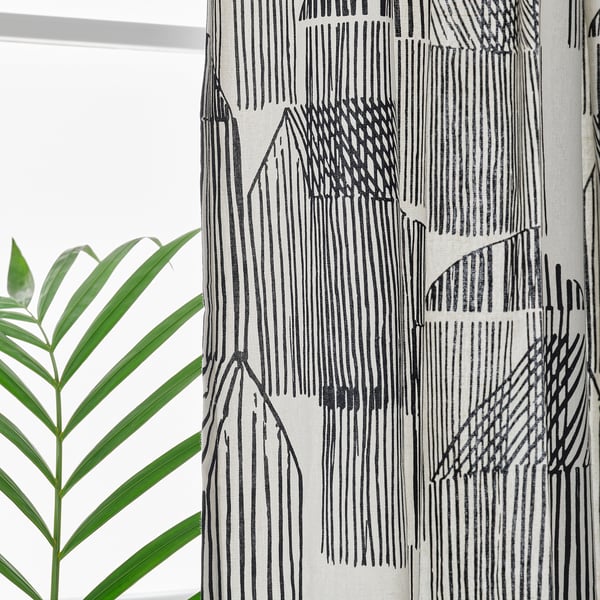 Black and white patterned curtains hang by a window, providing privacy and filtering light. A green plant leaf is visible on the left.