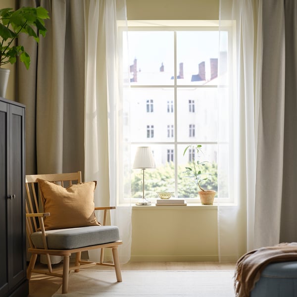 Cosy room with large window, beige TERESIA curtains, wooden chair, and small table with lamp and plant.