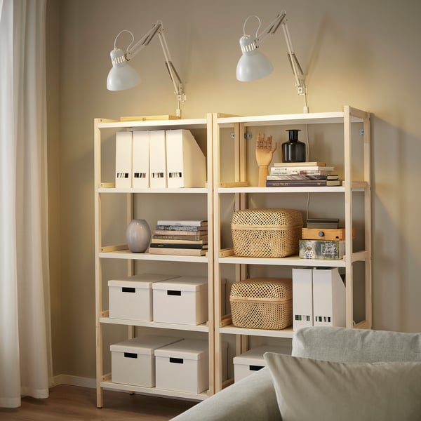 Two TERTIAL lamps on bookshelves illuminating books and boxes next to a beige couch.