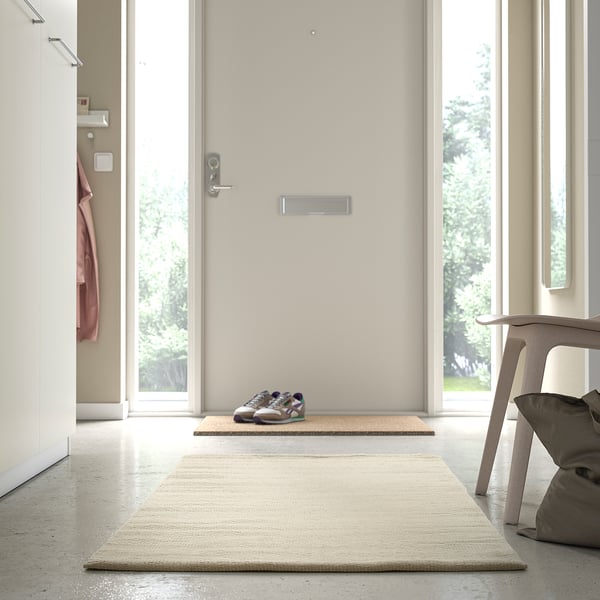 Modern room with beige TIDTABELL rug near door, smaller rug, and chair with cushion.