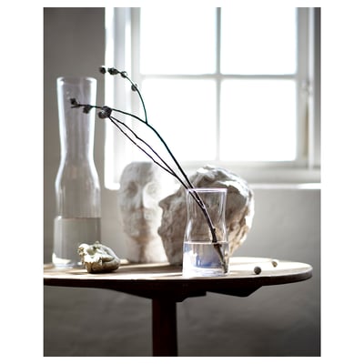 Clear glass vase with long-stemmed flowers and textured white vases on a table by a window.