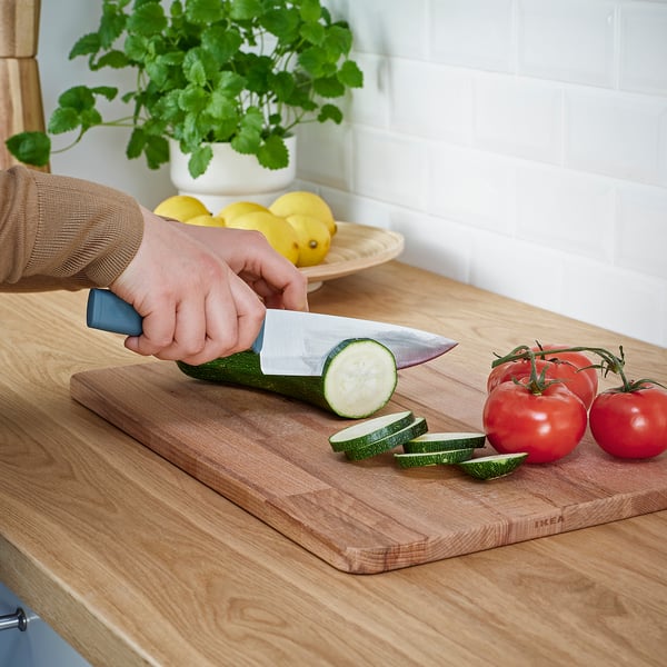 Person slicing courgette on wooden cutting board with a knife from the TIGERBARB set. Red tomatoes nearby.