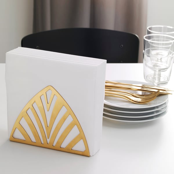 Gold napkin holder with white napkins, stacks of plates, and glasses on table.