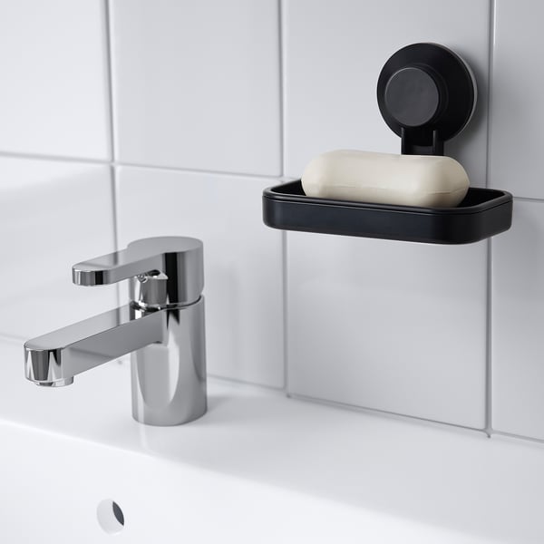 Small black TISKEN soap dish suctioned to tiled wall beside shiny chrome faucet, holding white soap.