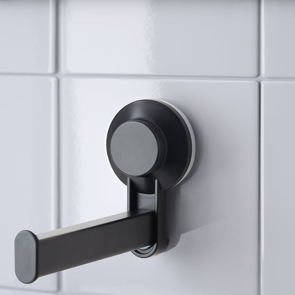 Black suction-cup mounted toilet paper holder on white tiles, easy to instal and remove without damaging walls.