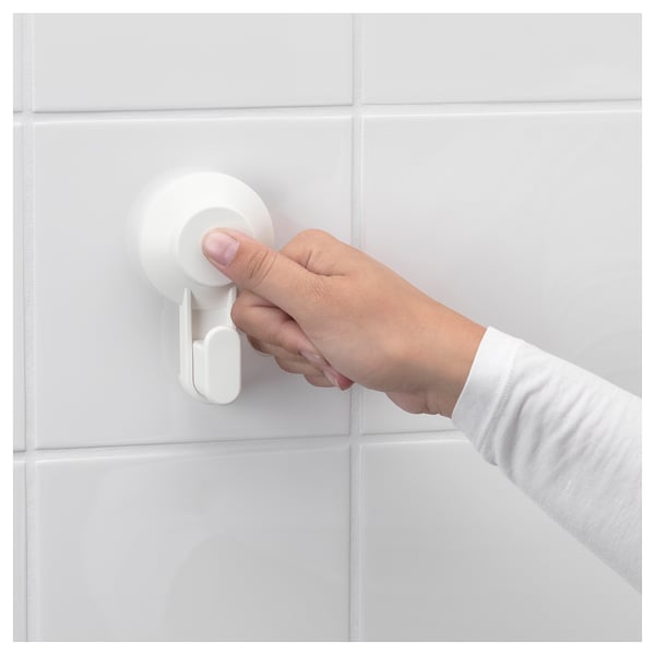 Hand pressing white TISKEN suction cup on white tiled wall.