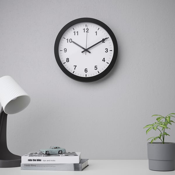 A modern black round wall clock with black numbers and hands, displaying time in a quiet room, indicating silence due to its silent quartz movement.