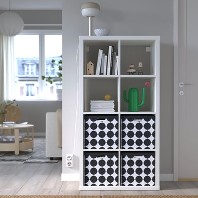 White TJENA box with black dots on shelf among books and decor.