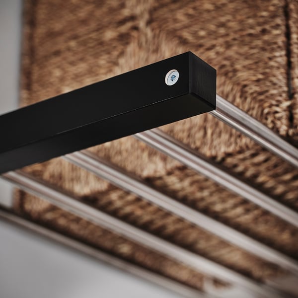 Black wooden coat rack with metal hooks on a rope wall background.