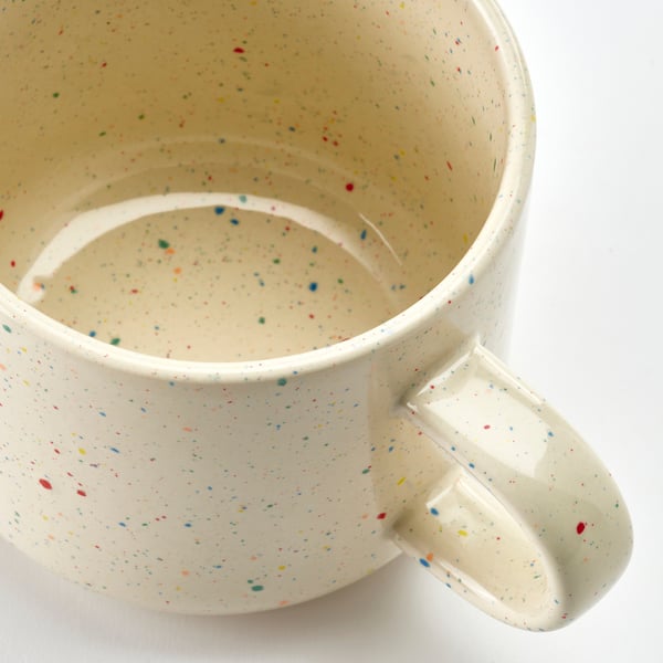 Speckled stoneware mug with handle, off-white base, multicoloured flecks, smooth texture, simple design.